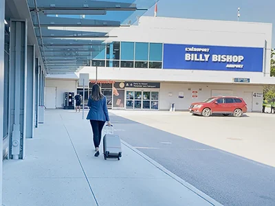 Une voyageuse avec une valise se dirige vers l’entrée continentale de l’Aéroport Billy Bishop.