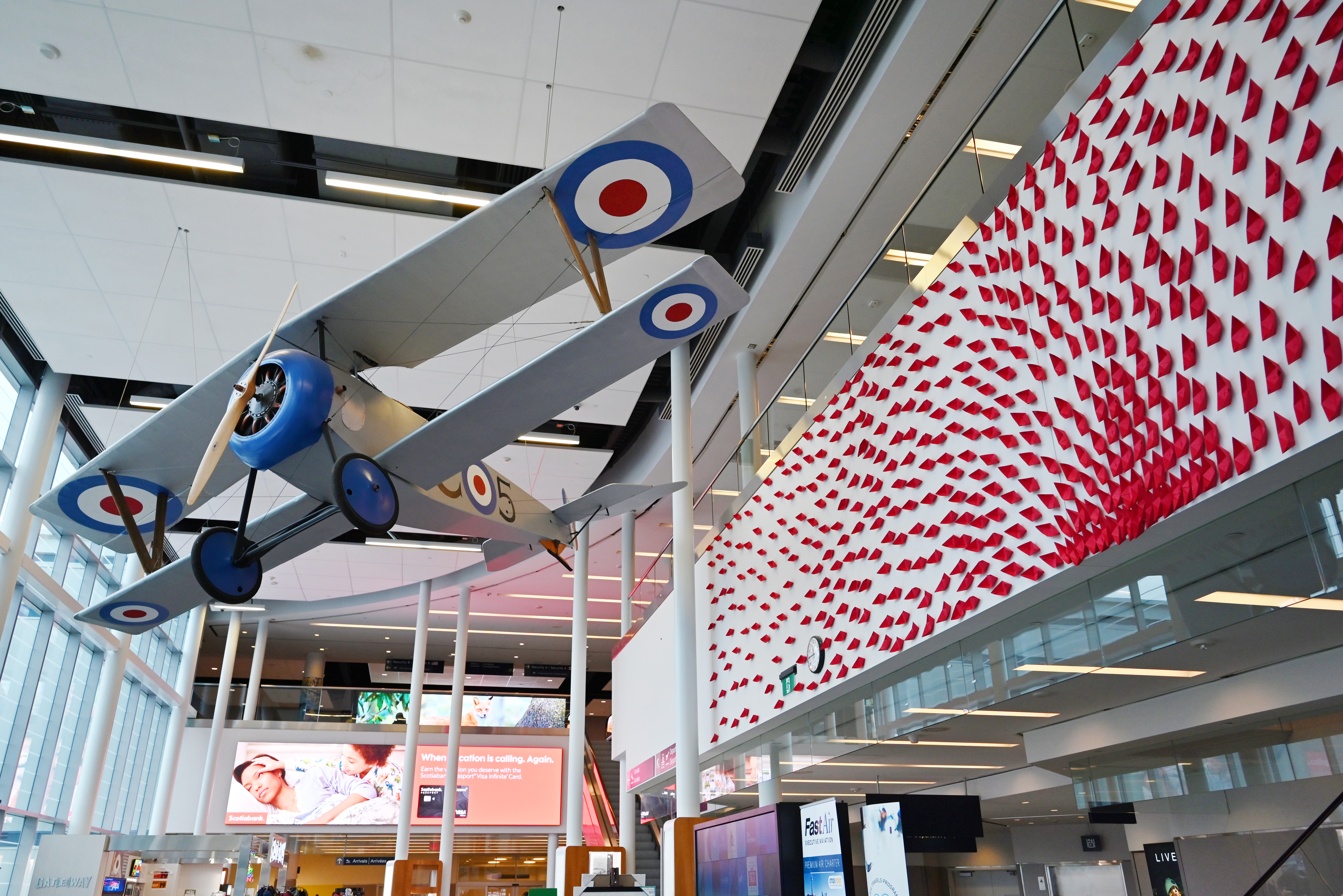 Une maquette de Nieuport 17 suspendue dans l’atrium de l’aéroport, près d’une installation textile rouge.