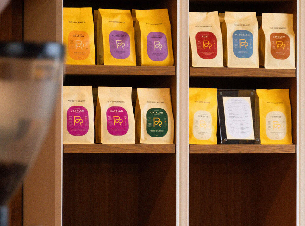 Des sacs de café Pilot Coffee Roasters exposés sur des étagères en bois.